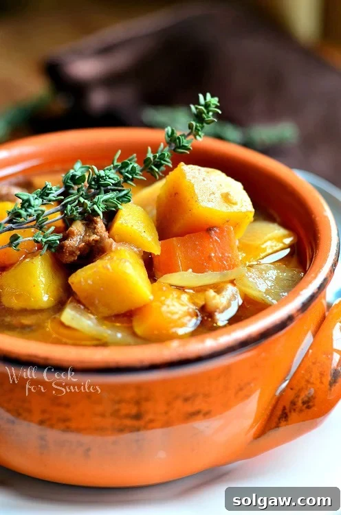 Hearty Slow Cooker Winter Squash Beef Stew in an orange bowl, garnished with a fresh sprig of rosemary.