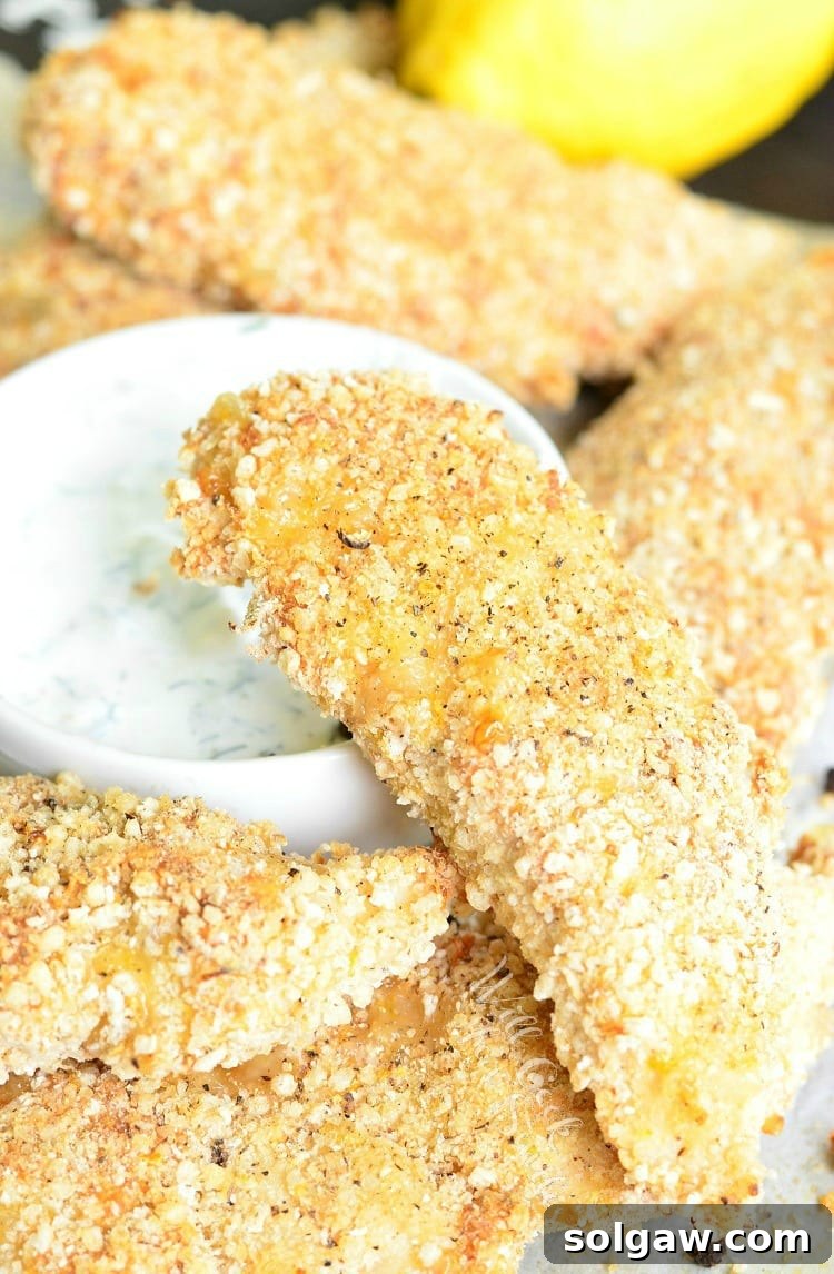 Lemon Pepper Baked Chicken Tenders stacked on a plate with dipping sauce in a white bowl