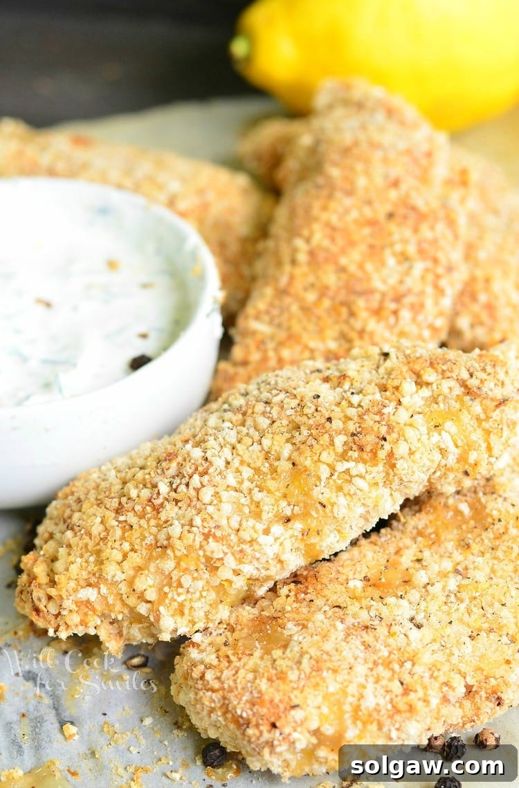 lemon pepper baked chicken tenders on a piece of wax paper with a white bowl of dipping sauce