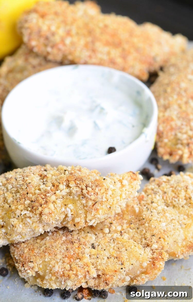 Lemon Pepper Baked Chicken Tenders on a baking dish with dipping sauce in a white bowl