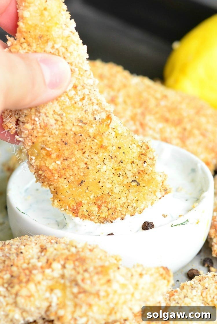 dipping Lemon Pepper Baked Chicken Tenders in sauce that is in a white bowl