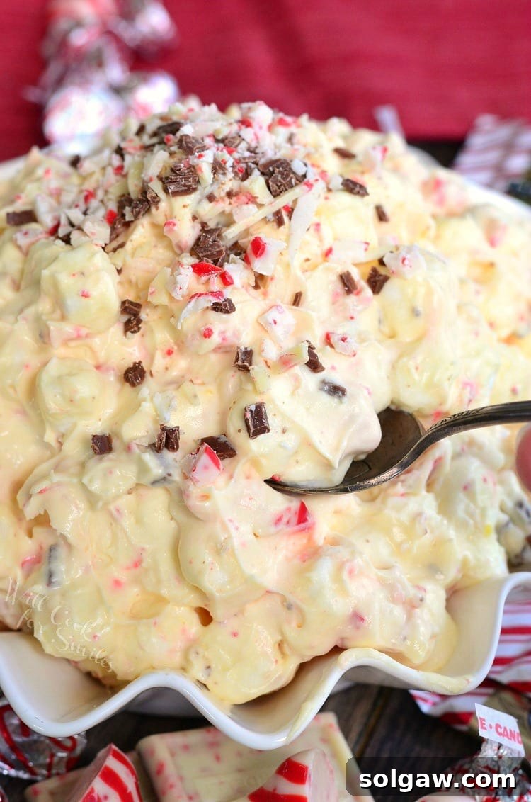 A scoop of White Chocolate Peppermint Fluff Salad with a spoon in a white bowl, capturing its light and airy texture.