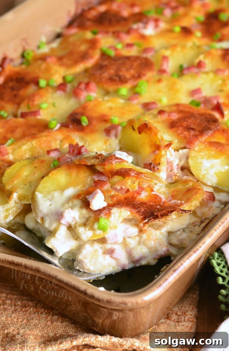 Chicken Cordon Bleu Scalloped Potatoes in a brown casserole dish with a spatula lifting a piece out, showing gooey cheese and tender potatoes