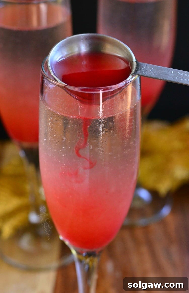 Raspberry Italian Champagne Spritz 3 Hand pouring homemade raspberry vanilla syrup into a champagne flute on a table, preparing a Raspberry Italian Soda Champagne Cocktail.
