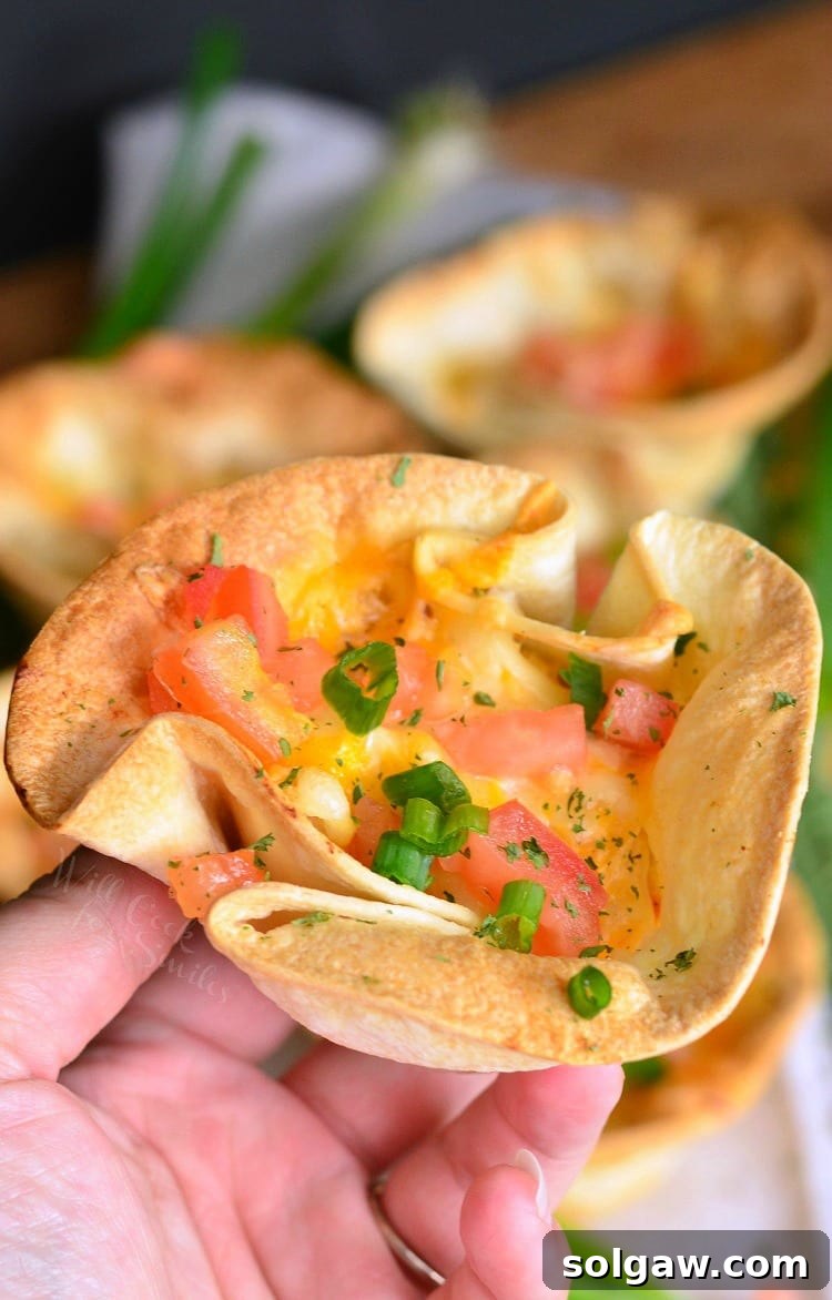 Close-up of a hand holding an enchilada cup topped with tomatoes and green onions