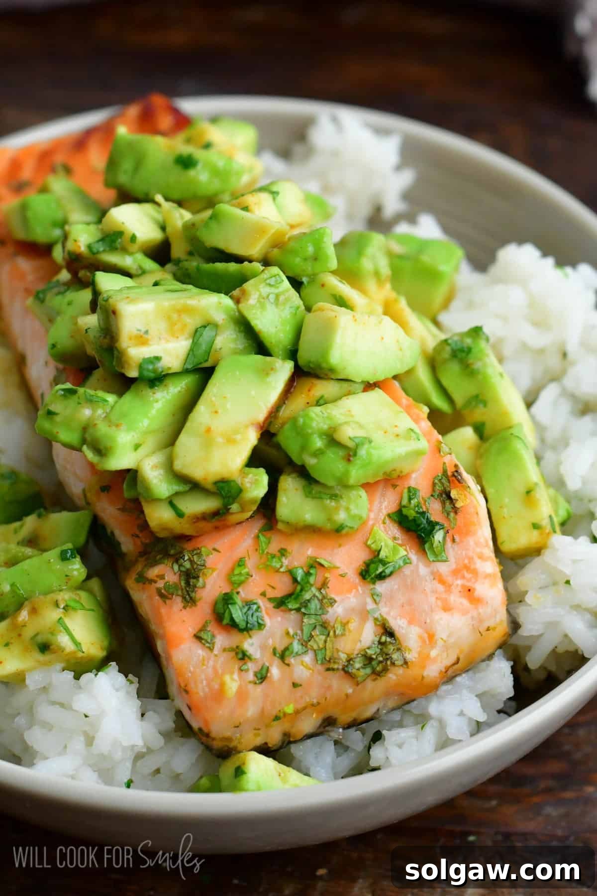 Beautifully baked salmon over a bed of fluffy rice, generously topped with a fresh avocado mixture, garnished with vibrant cilantro.