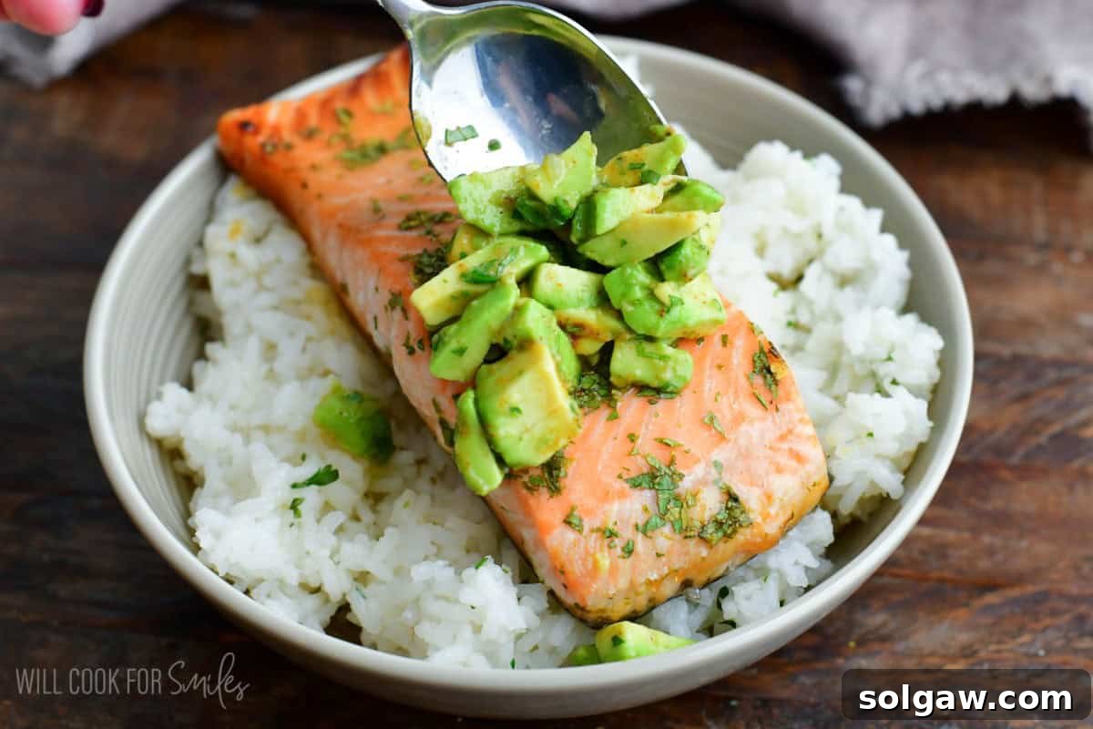 Adding a scoop of vibrant green avocado topping onto a cooked salmon fillet in a rice bowl, ready to serve.