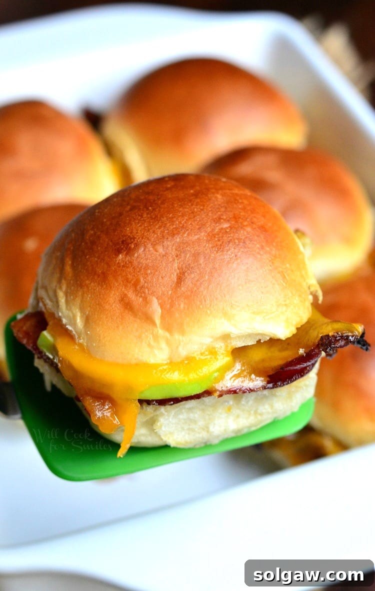 An Apple Bacon Cheddar Slider being lifted from a white baking dish with a green spatula, showcasing its layers.