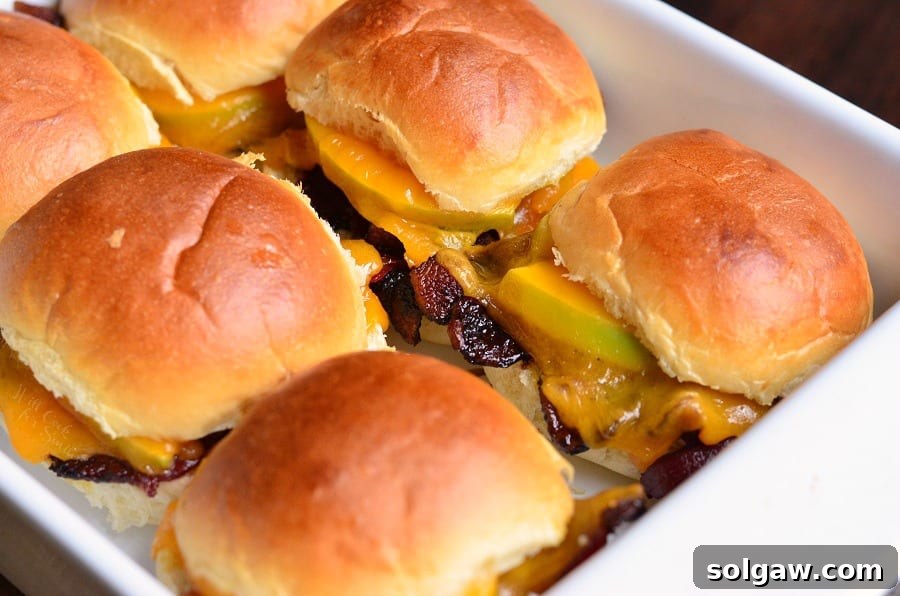 A close-up of Apple Bacon Cheddar Baked Sliders in a baking dish, highlighting the melted cheese and crispy bacon.