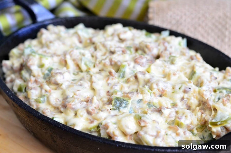 Cheesy Sausage Peppers and Onions Dip served warm in a small cast iron pan, garnished and ready for guests