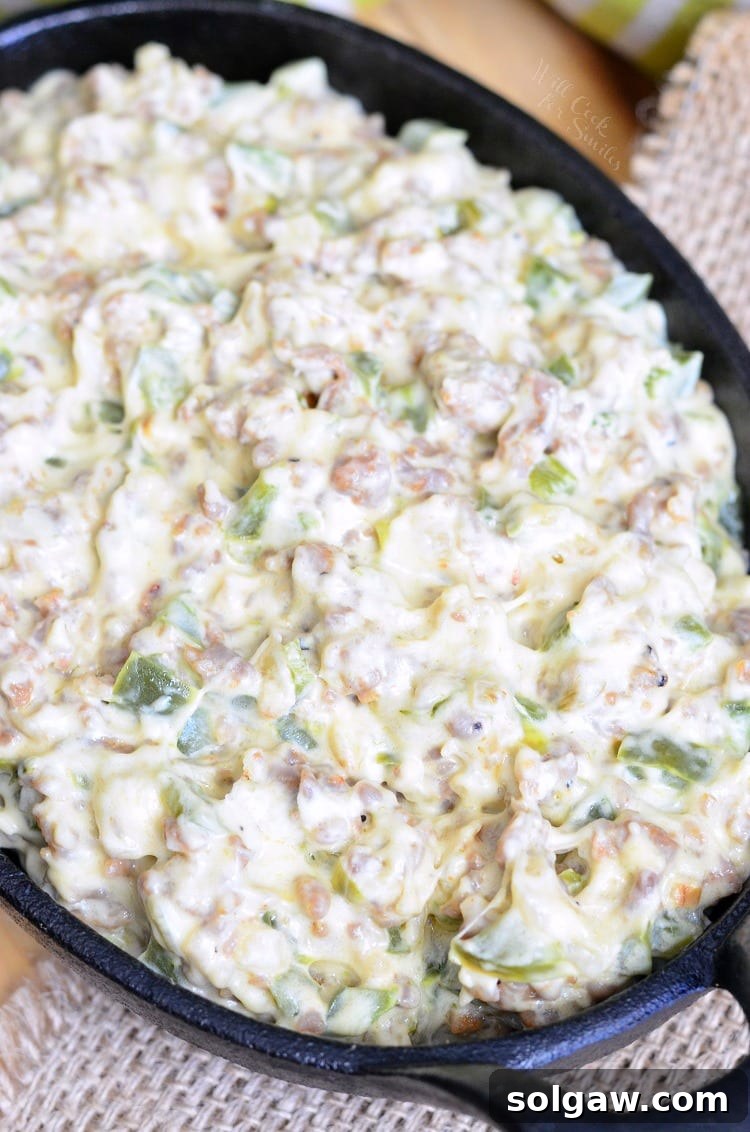 Top view of Cheesy Sausage Peppers and Onions Dip in a cast iron pan, showcasing its rich texture, melted cheese, and fresh ingredients