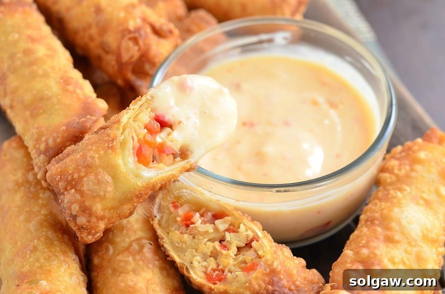 Sweet Chili Chicken Egg Rolls with Creamy Sweet Chili Sauce in a glass bowl with some sauce on one of the rolls
