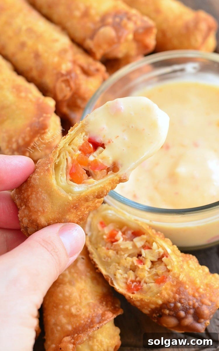 Dipping Sweet Chili Chicken Egg Rolls in a Creamy Sweet Chili Sauce that is in a clear glass bowl