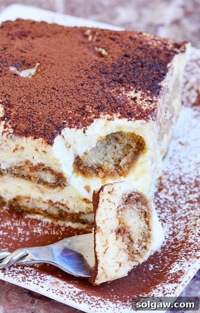 A single serving of classic Tiramisu on a white plate, with a fork lifting a perfect bite