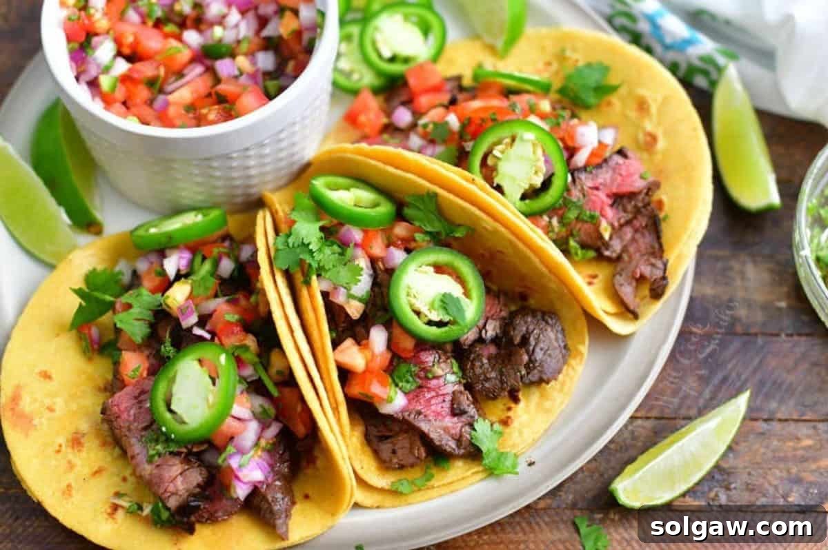 Three beautifully arranged carne asada tacos on a plate, garnished with fresh cilantro and lime wedges, with a side bowl of pico de gallo, showcasing a perfect meal.