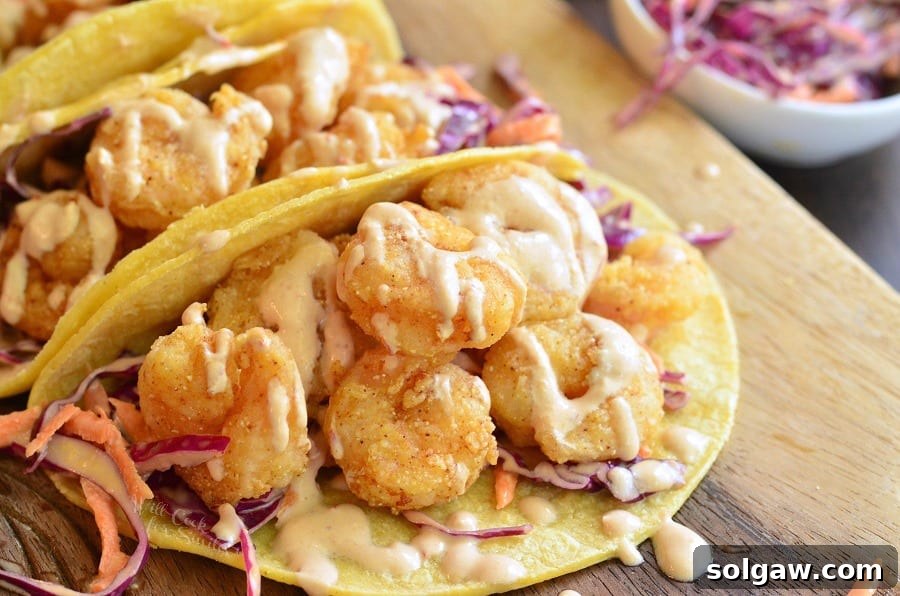 Horizontal shot of a crispy shrimp taco, topped with sour cream, on a rustic wooden board.