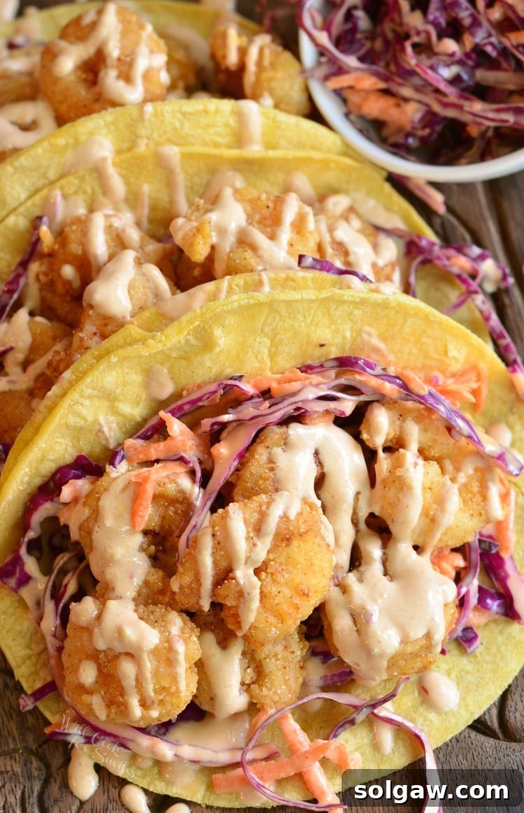 Three corn tortillas filled with crispy shrimp and vibrant red cabbage slaw, artfully arranged on a wooden cutting board, ready for serving.