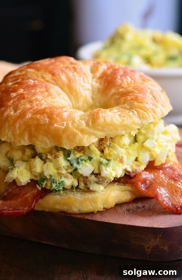 Bacon and Green Onion Egg Salad on a croissant on a cutting board