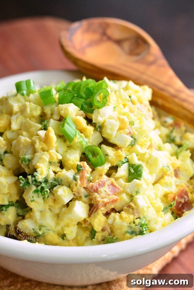 Bacon and Green Onion Egg Salad in a white bowl with a wooden spoon across the top