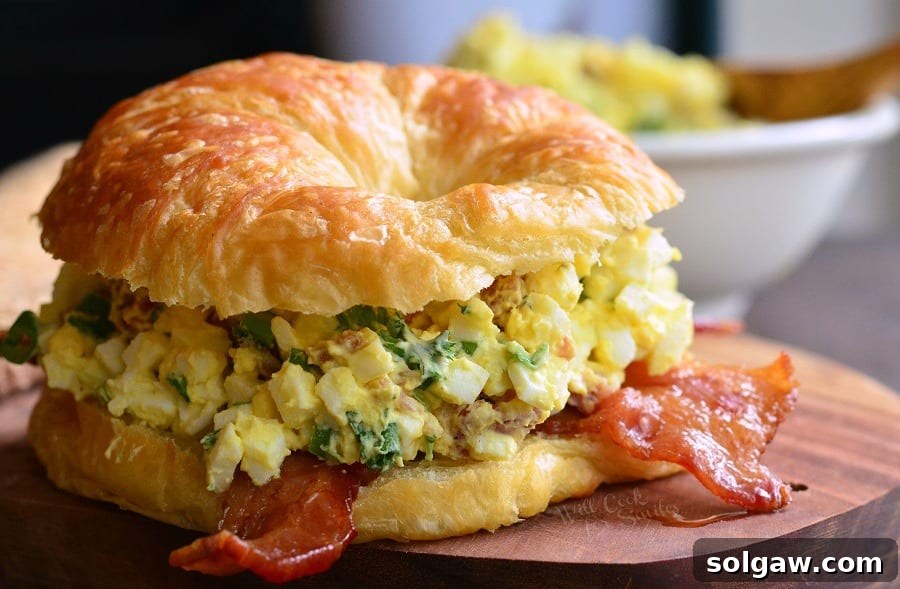 horizontal image of Bacon and Green Onion Egg Salad on a croissant on a cutting board