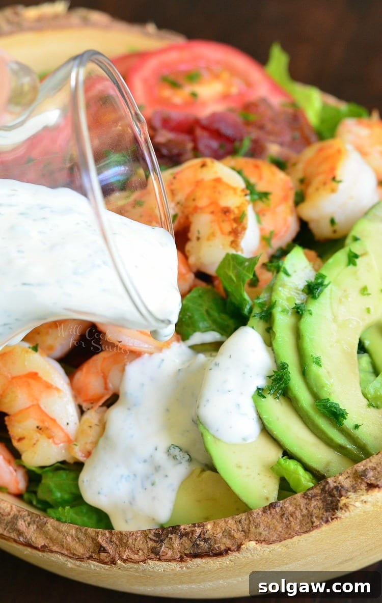 Buttermilk Ranch dressing being poured generously over a fresh Shrimp BLTA Salad