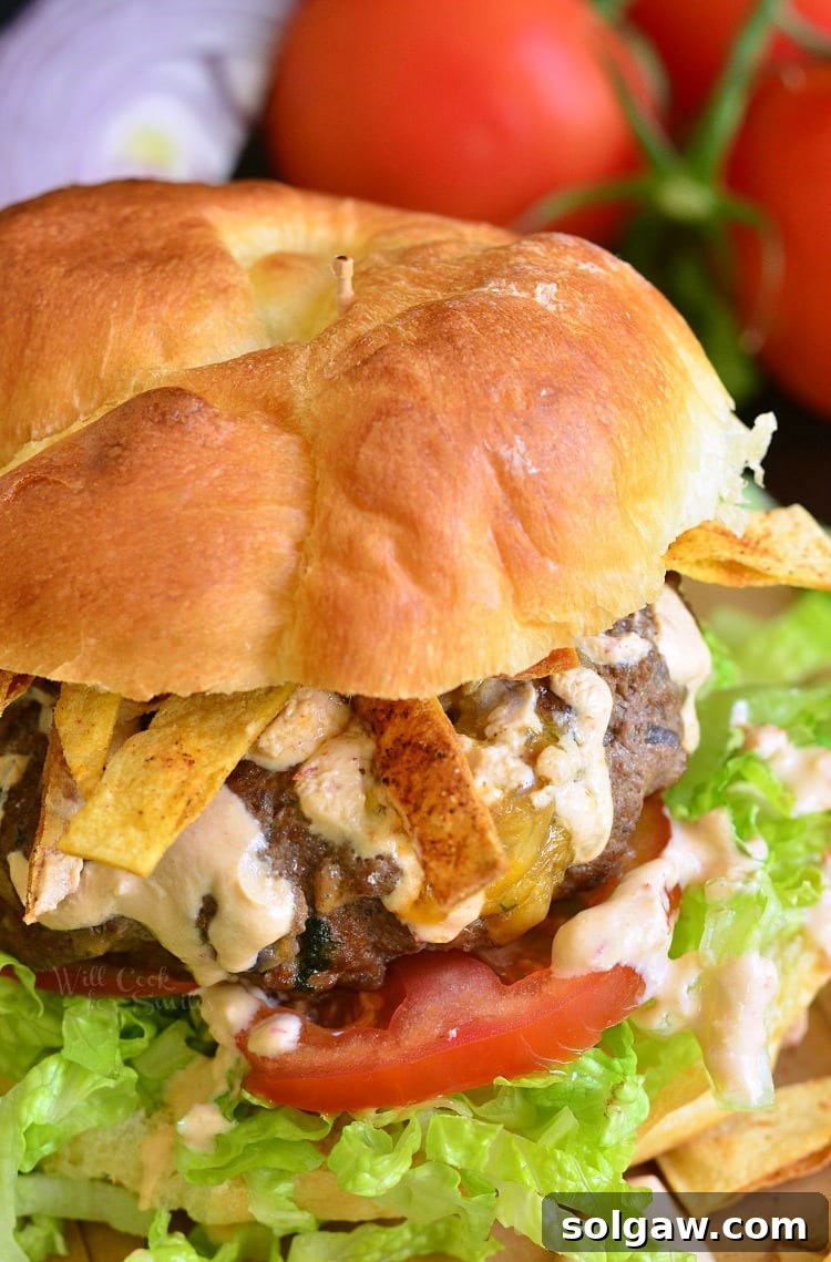 A delicious Stuffed Taco Burger on a fluffy bun with fresh lettuce and tomato, with a background blur of additional tomatoes, ready to be devoured.