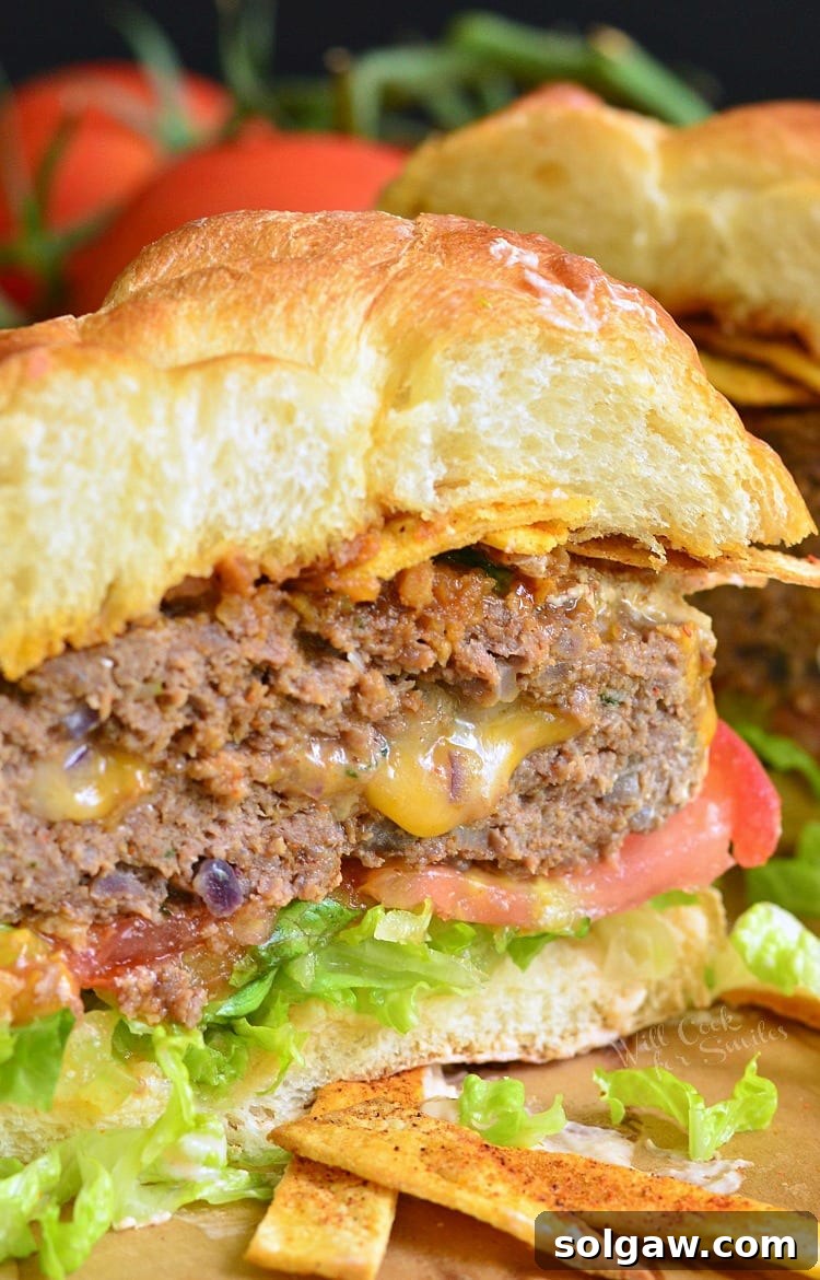 A delectable Stuffed Taco Burger, sliced in half to reveal its cheesy interior, served on a bun with crisp lettuce and a fresh tomato slice, showcasing its irresistible appeal.