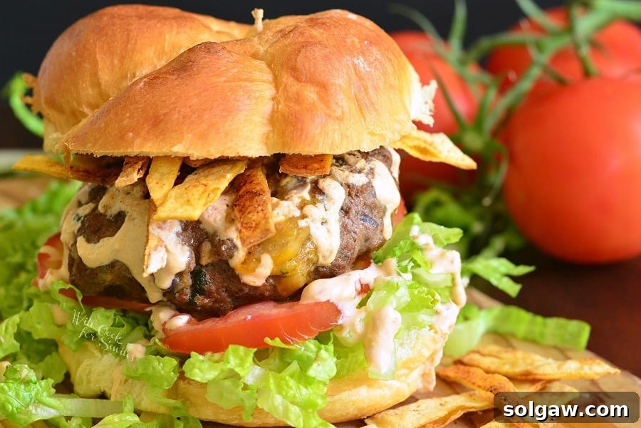 A close-up shot of a Stuffed Taco Burger on a bun with fresh lettuce and tomato, capturing its vibrant colors and inviting texture, with tomatoes out of focus in the background.