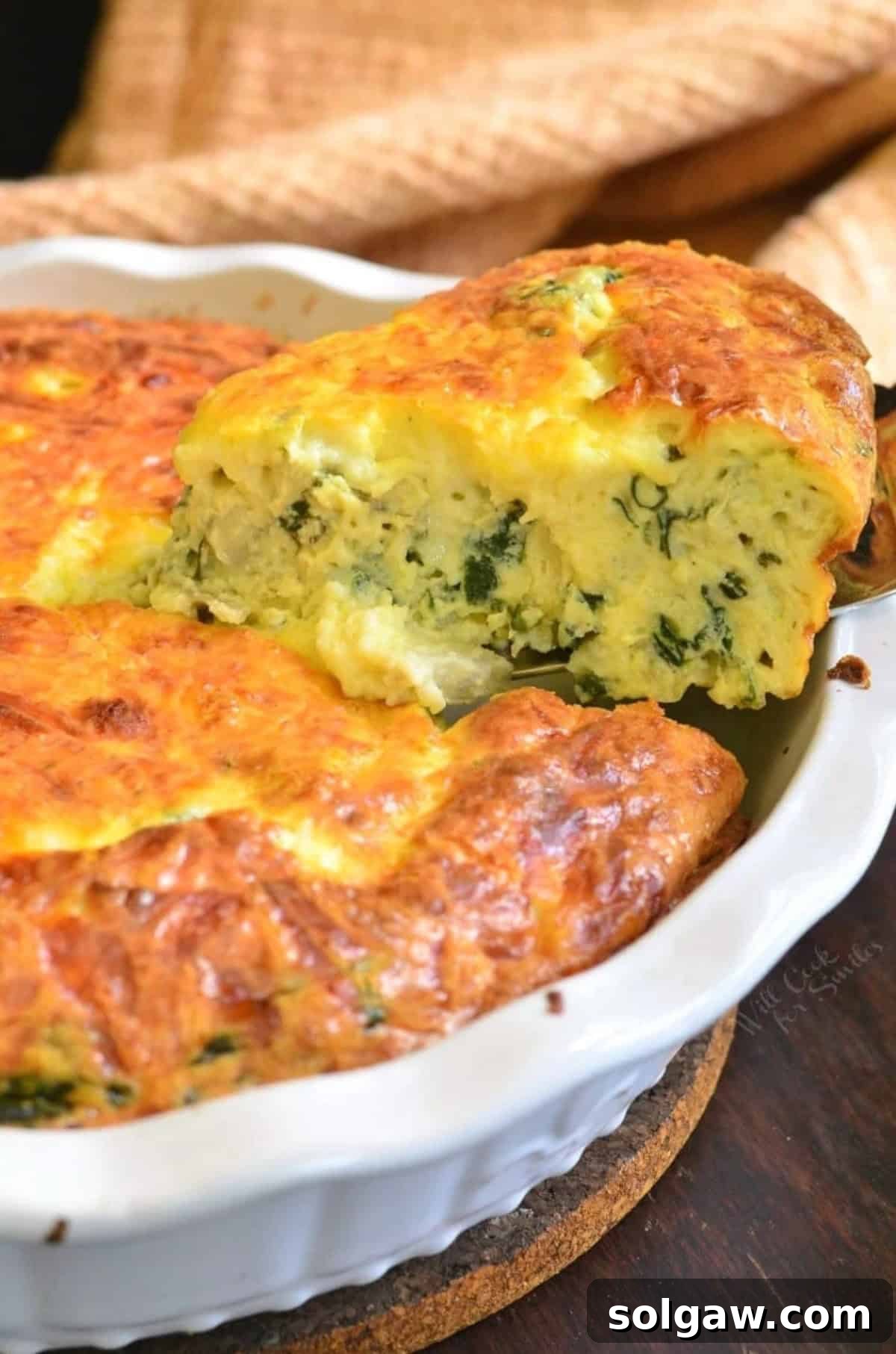 A golden-brown slice of spinach artichoke crustless quiche being pulled from a baking dish, showcasing its fluffy interior.