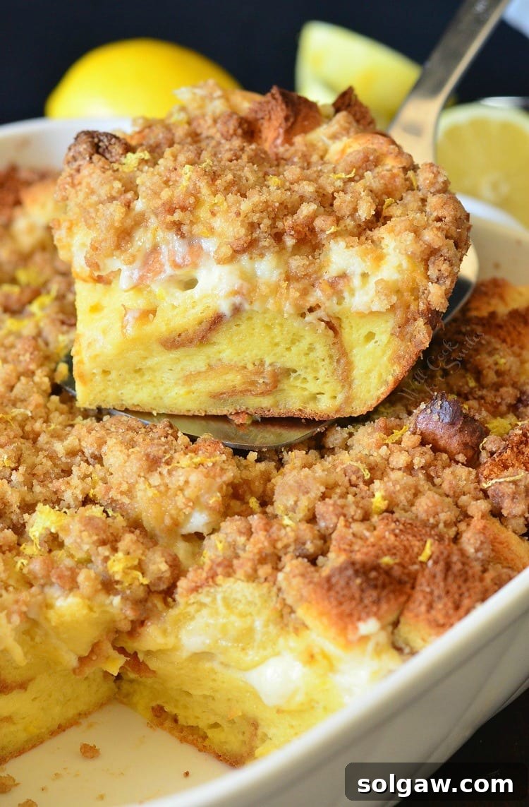 A golden-brown Lemon Cheesecake French Toast Casserole in a baking dish, with a generous slice lifted on a spatula, revealing creamy cheesecake layers and golden crumble.