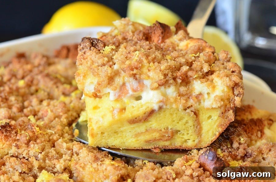 An overhead shot of the baked Lemon Cheesecake French Toast Casserole in a rectangular dish, with one serving removed, showcasing its delicious texture and golden crumble topping.