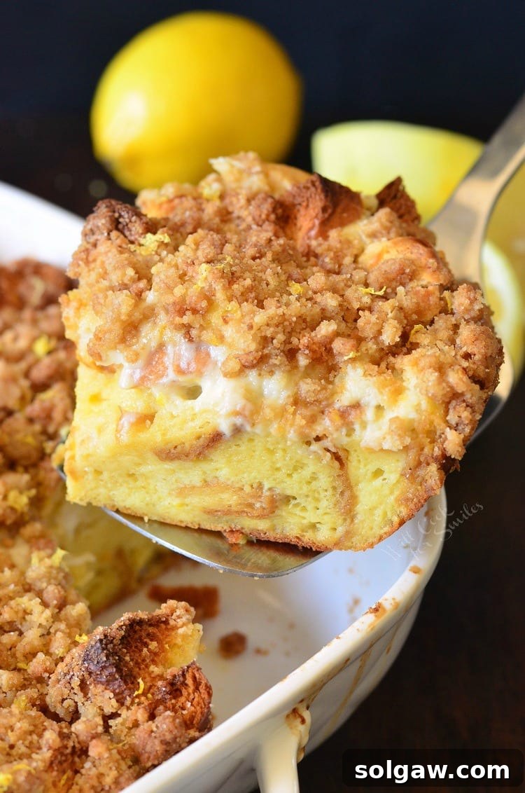 A large, inviting slice of Lemon Cheesecake French Toast Casserole perfectly lifted on a spatula, showcasing its fluffy brioche base, creamy cheesecake filling, and crunchy lemon crumble.