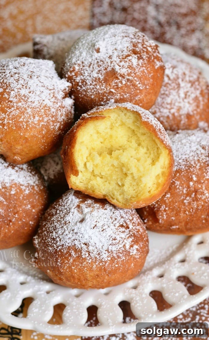 Easy Ricotta Doughnuts generously piled on a decorative round white plate, beautifully dusted with powdered sugar, with one doughnut having a bite taken out to reveal its soft interior.