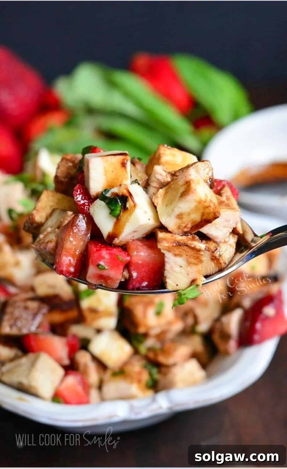 A spoon is lifting a portion of Balsamic Strawberry Chicken Salad above the bowl, showcasing the vibrant ingredients.