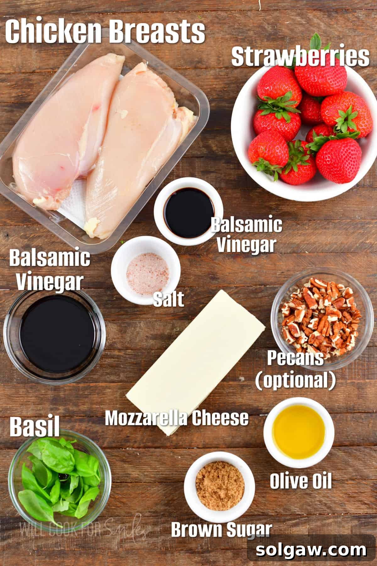 A carefully arranged display of labeled ingredients, including chicken breasts, balsamic vinegar, fresh mozzarella, ripe strawberries, and basil, set against a rustic wooden background for making balsamic chicken salad.
