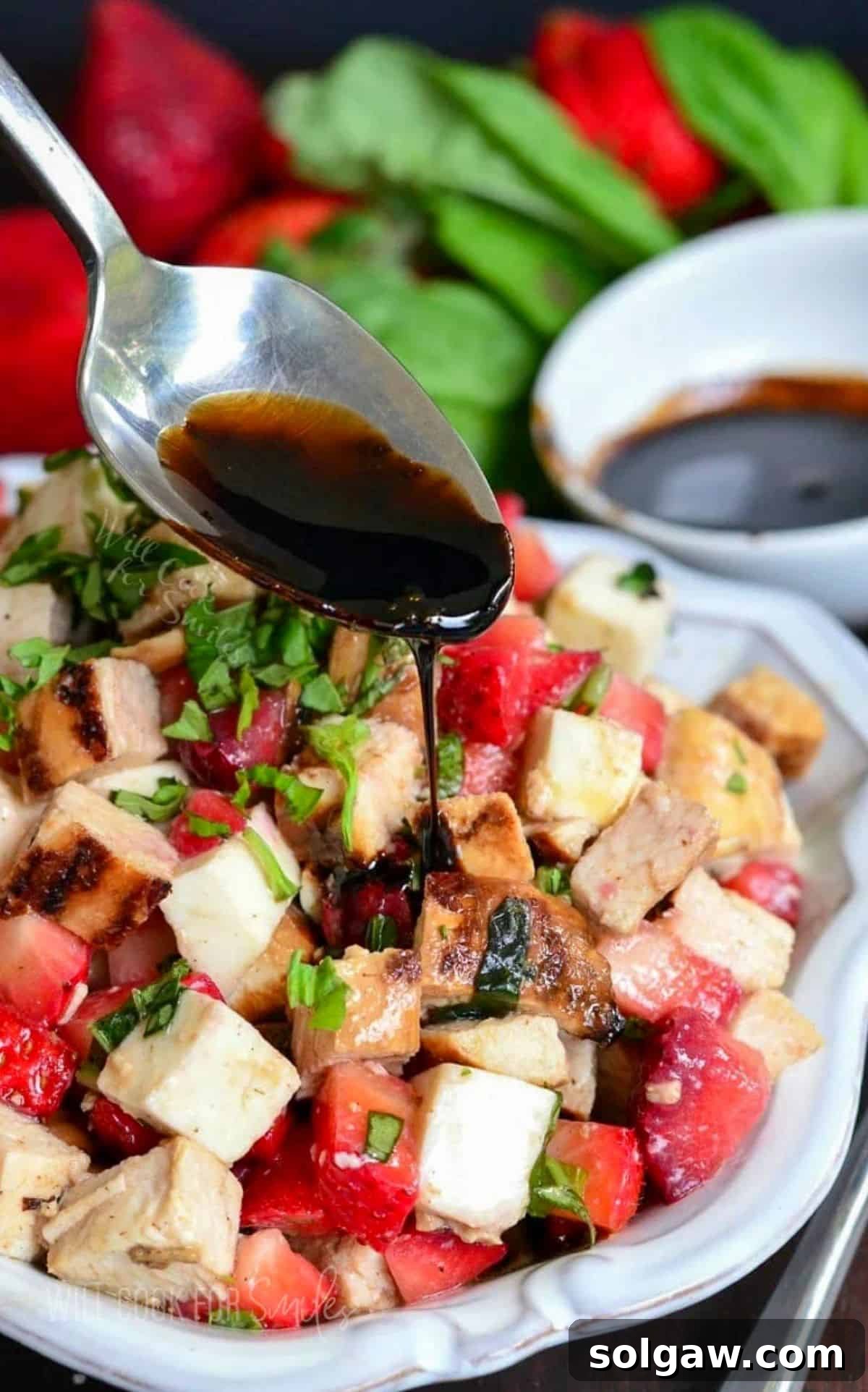 Balsamic reduction is being delicately poured over a beautifully arranged chicken strawberry salad, ready to be served.