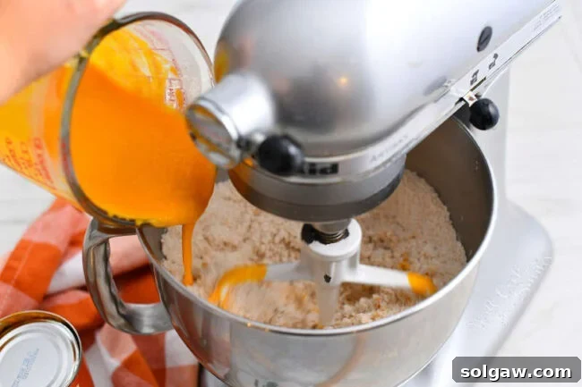 adding pumpkin puree mixture to bowl of a stand mixer with flour in it
