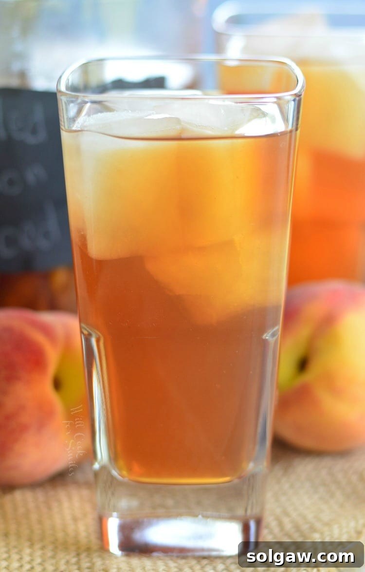 Grilled Lemon Peach Iced Tea in a glass with ice and peaches in the background 