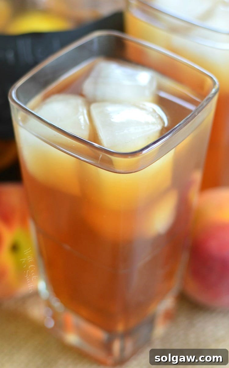 Top view Grilled Lemon Peach Iced Tea in a glass with ice and peaches in the background 