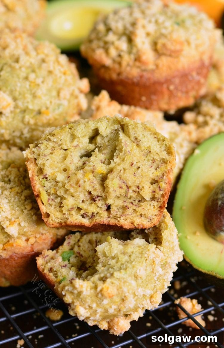 Freshly baked Avocado Banana Muffins cooling on a rack with a ripe avocado in the background, hinting at the key ingredient.