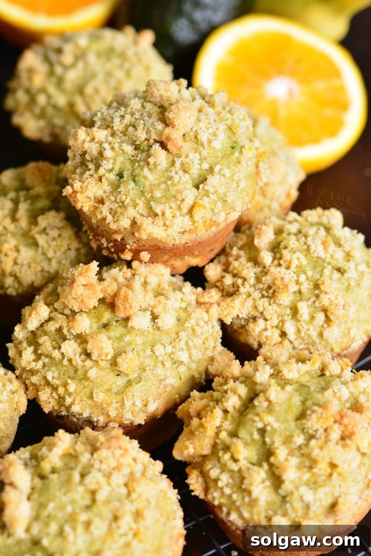 A beautiful stack of Avocado Banana Muffins with Orange Streusel on a wooden board, with a fresh orange in the background, subtly highlighting the citrus notes and fresh ingredients.