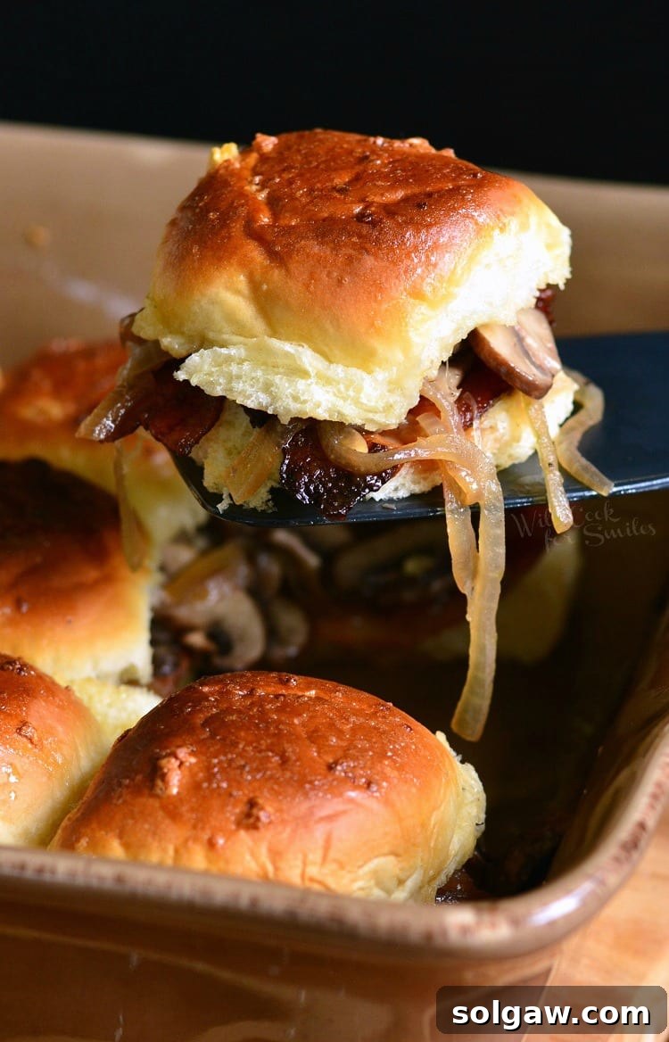 Bacon Mushroom and Onion Sliders being lifted out of baking dish with a spatula 