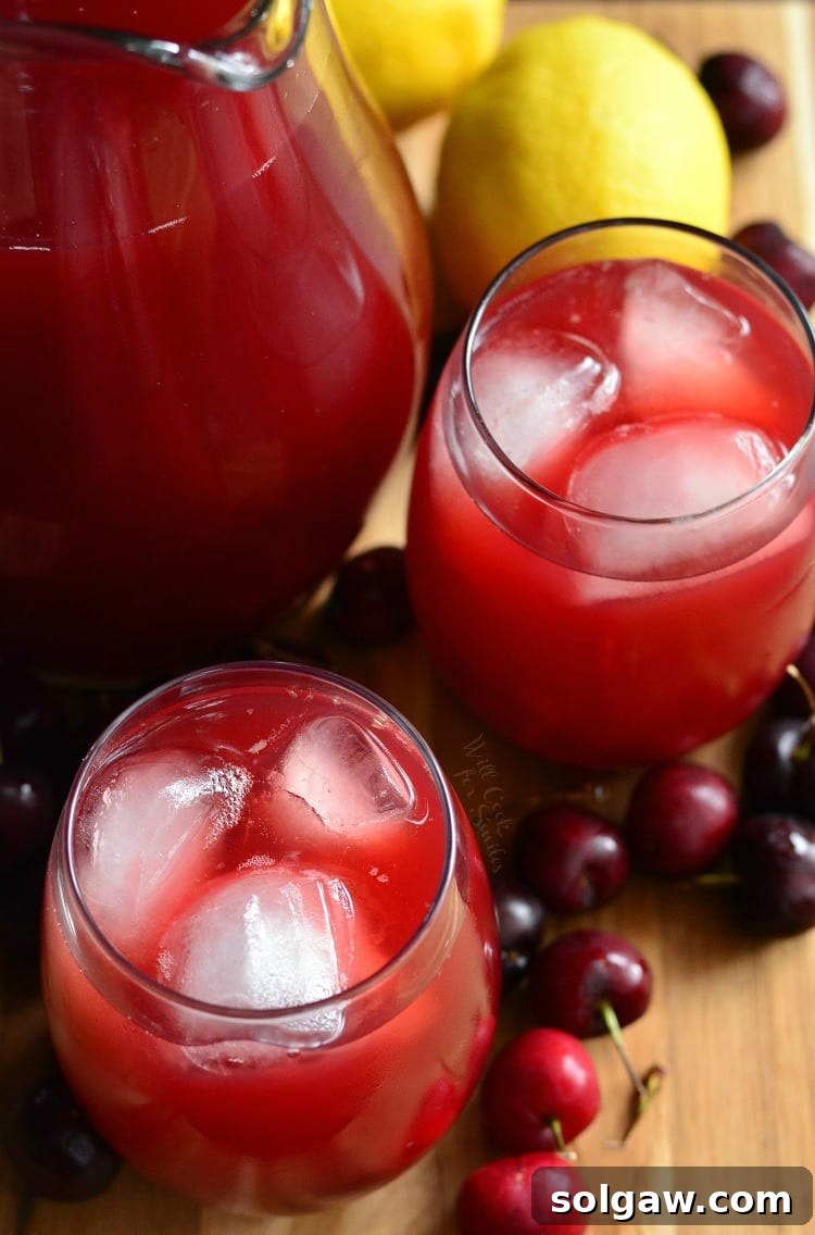 Top view of Cherry Arnold Palmer in glasses with a pitcher to the left of them with cherries around them and lemons on a cutting board 