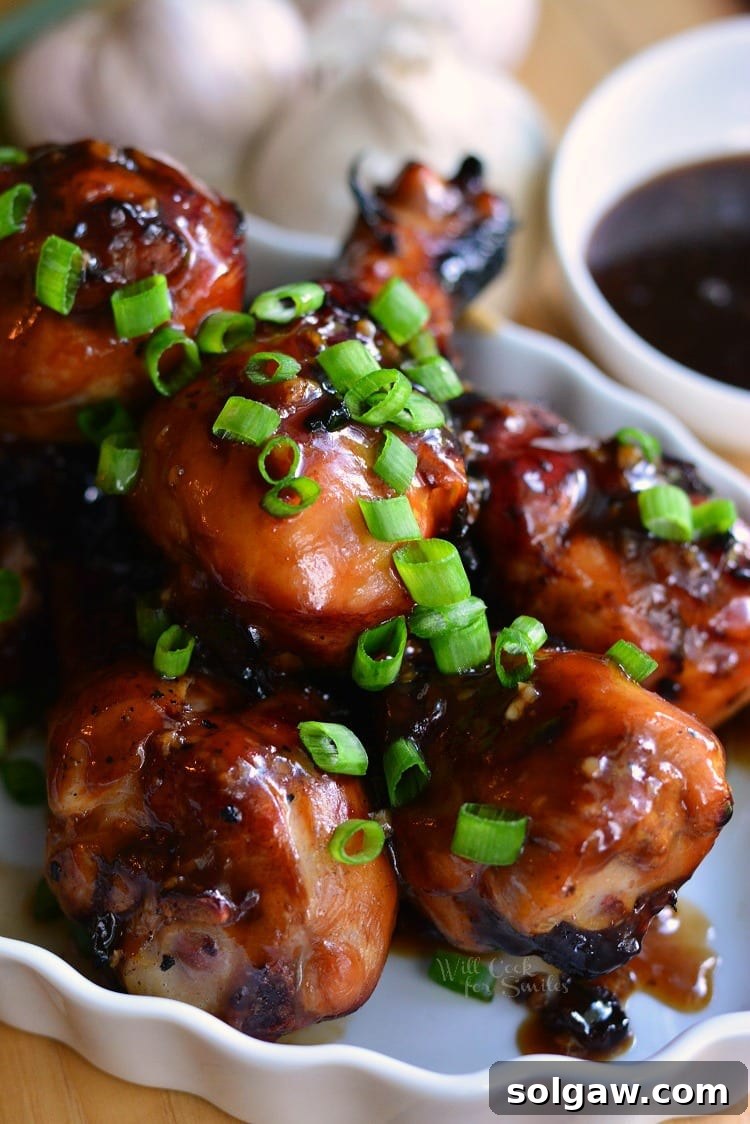 Sweet Garlic Grilled Chicken Drumsticks on a serving plate with fresh garlic cloves and a bowl of sweet garlic sauce in the background, showcasing the delicious glaze.