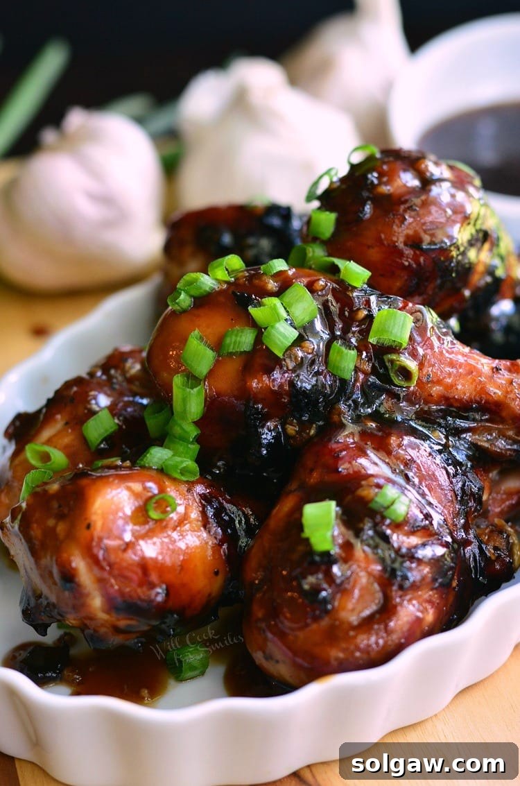 Sweet Garlic Grilled Chicken Drumsticks with fresh green onions sprinkled on top, arranged on a serving plate with garlic cloves and sauce in the background.