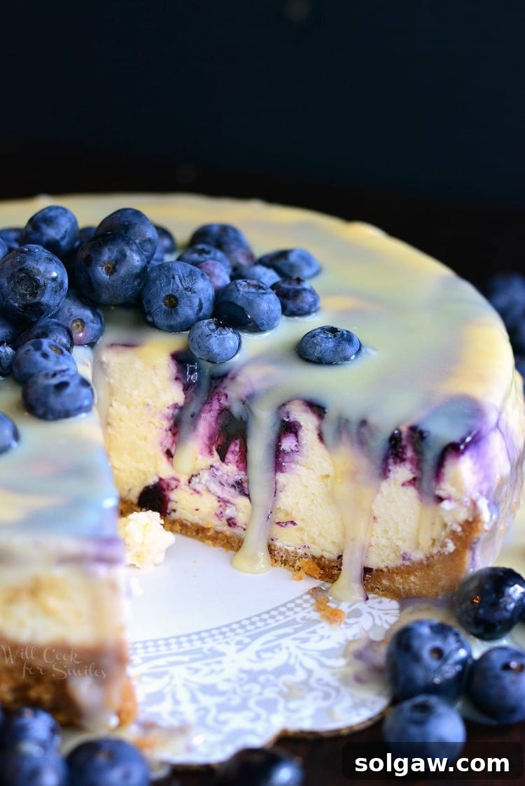 A decadent slice of white chocolate blueberry cheesecake topped with fresh blueberries and a drizzle of white chocolate ganache.
