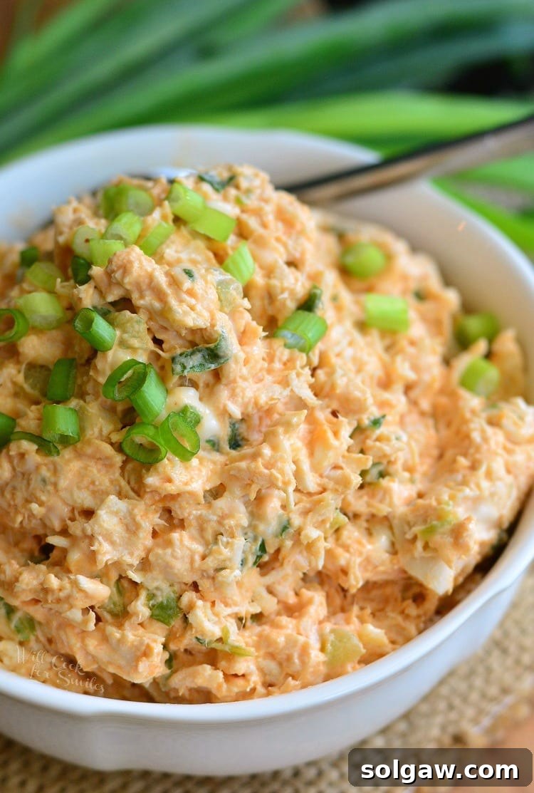 Zesty Buffalo Chicken Salad in a white bowl with green onions on top with a spoon, highlighting its vibrant appeal and delicious textures