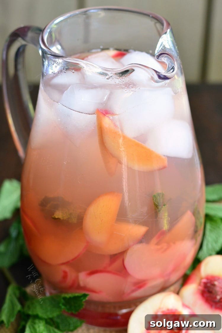 Blushing Peach Rose Mint Sparkler 6 Close-up photo of fresh mint and sliced peaches infusing in rosé wine in a glass pitcher.
