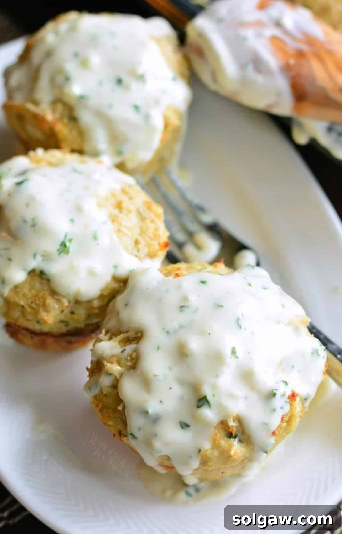 Parmesan Garlic Chicken Mini Loaves 7 Three mini chicken meatloaves with cream sauce on top on a long plate.