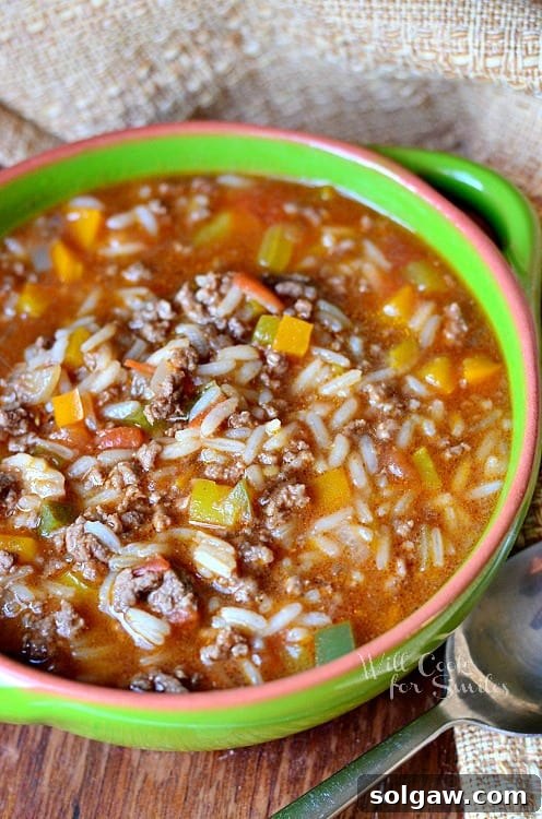 stuffed pepper soup in a green bowl with a spoon next to the bowl sitting on a table  